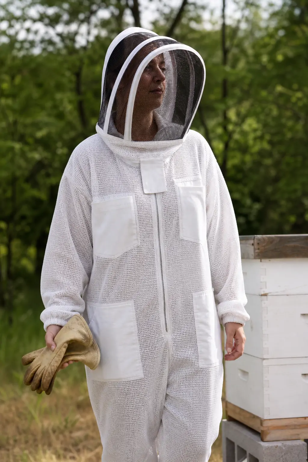 A beekeeper wearing a ventilated protective suit and veil while holding leather gloves.